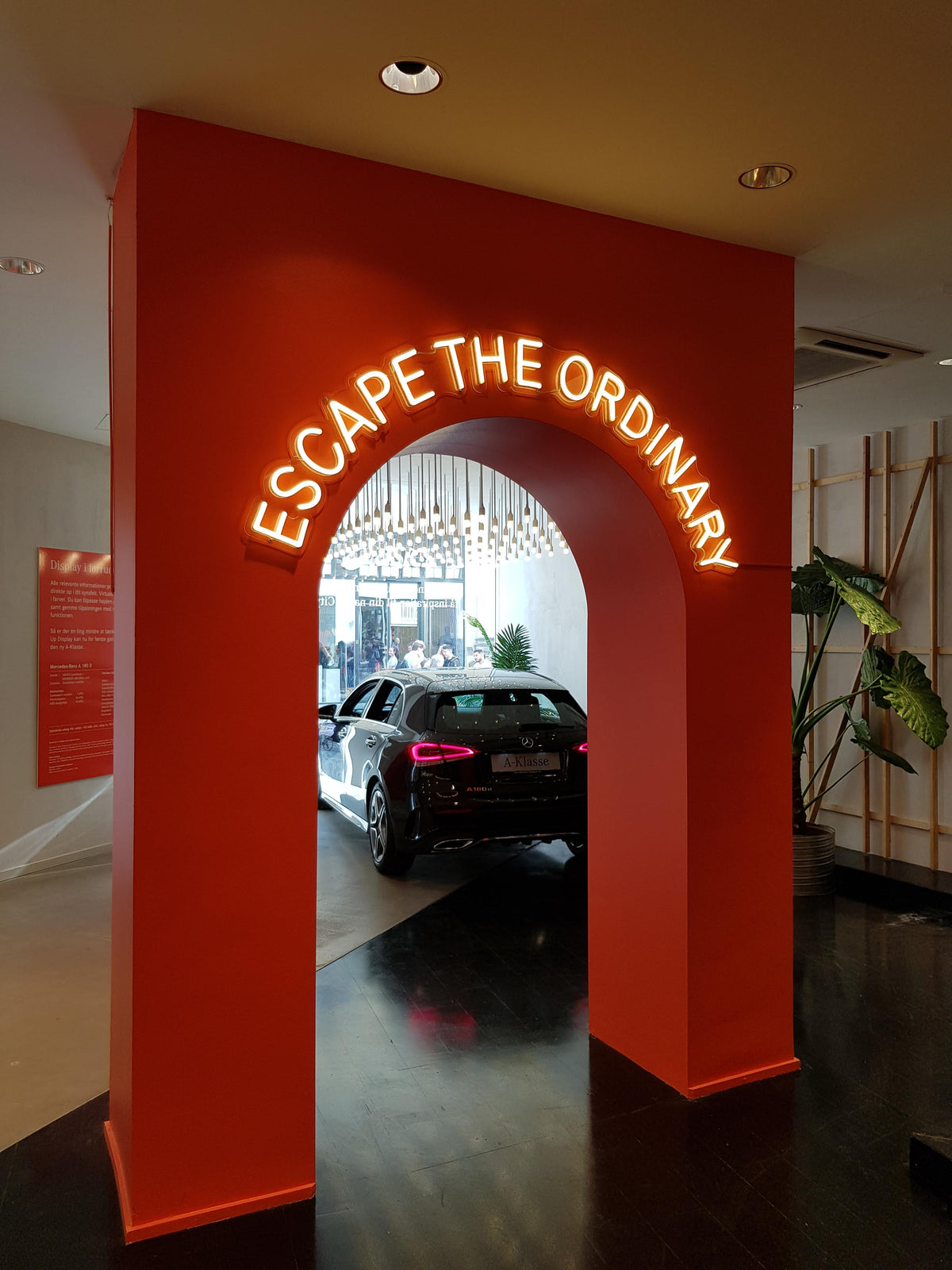 Neontekst med ESCAPE THE ORDINARY på en orange bue ved en bilpræsentation