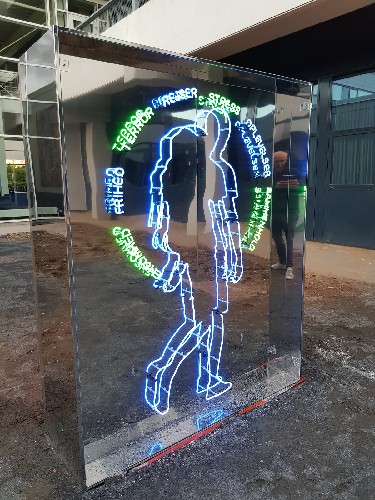 Spejlskulptur med en neonfigur og ord i blå og grøn