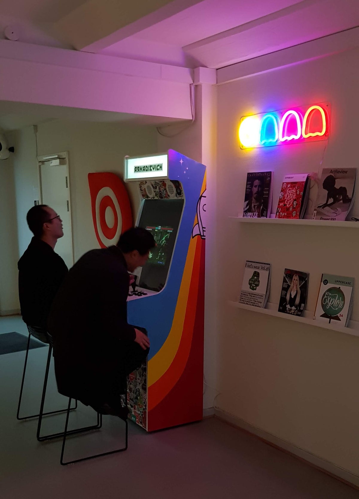 Spøgelser i neonfarver over en hylde ved en arkademaskine i en kontorlounge