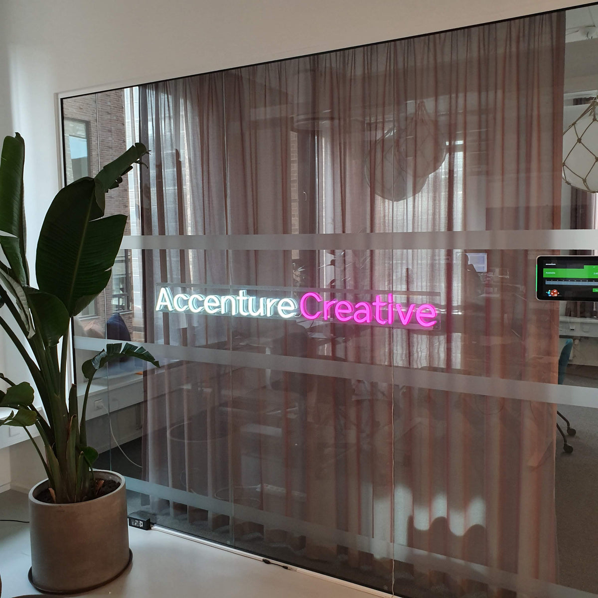 Accenture Creative-logo i hvid og pink neon på en glasvæg