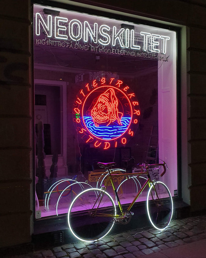Butiksvindue med NEONSKILTET-skilt og et rødt og blåt hajlogo i neon