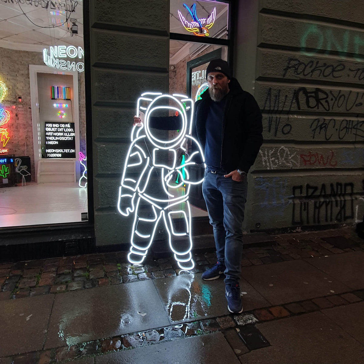 Hvid neonastronaut foran et butiksvindue på gaden