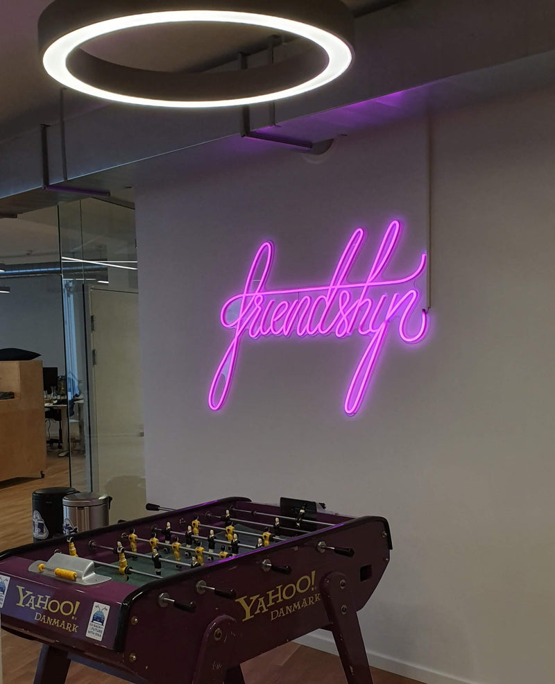 Pink neonskilt med friendship over et bordfodboldspil på et kontor