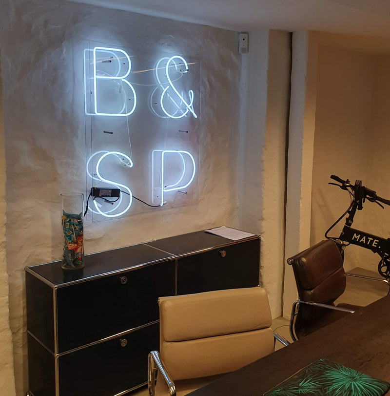 Hvidt neonskilt med B&amp;SP over en reol på et kontor