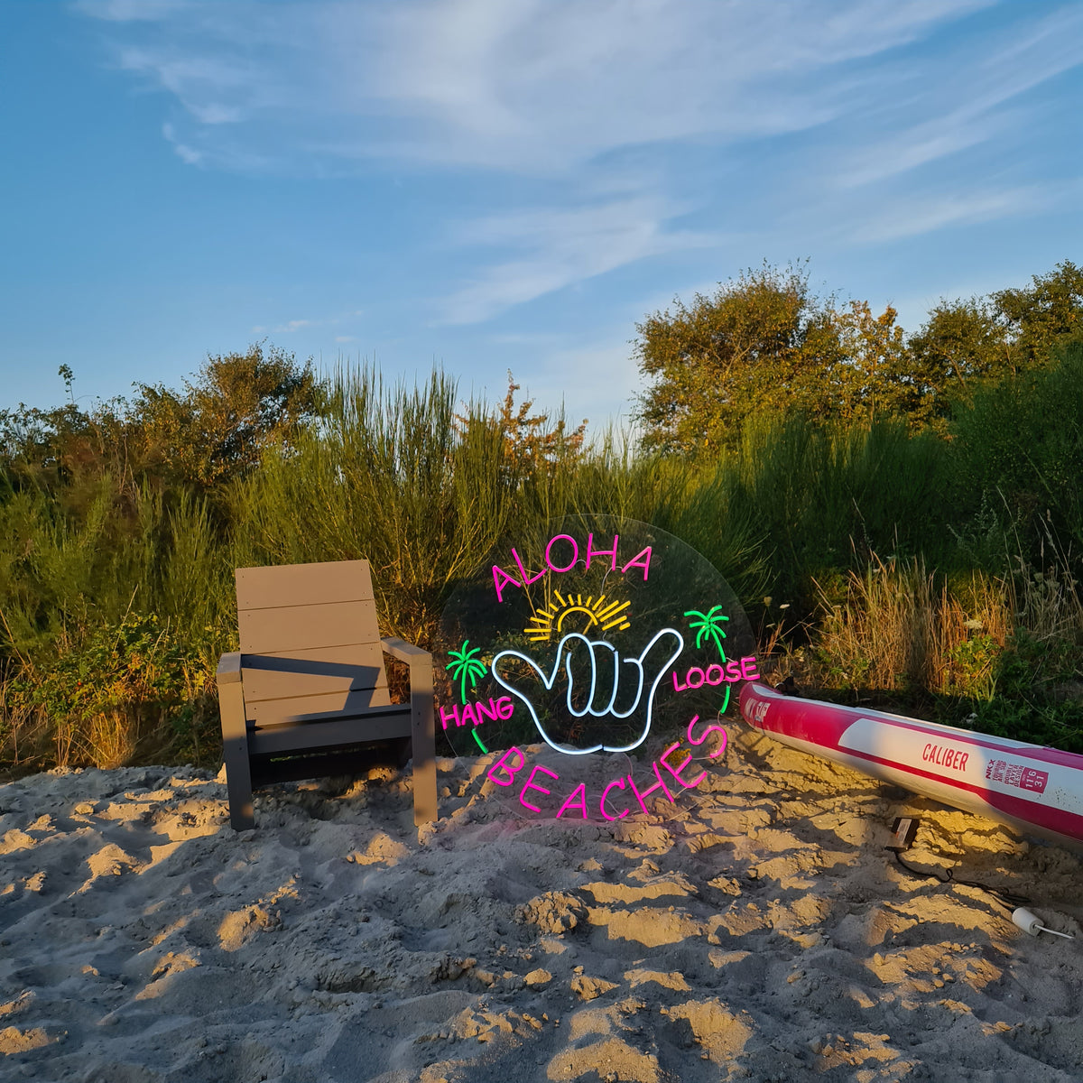Neonskilt med ALOHA BEACHES og en hang loose-hånd på en strand