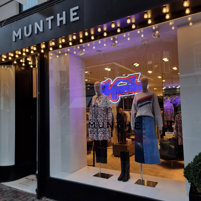 Neonskilt med Munthe-logoet i blåt og rødt i butiksvinduet hos Munthe