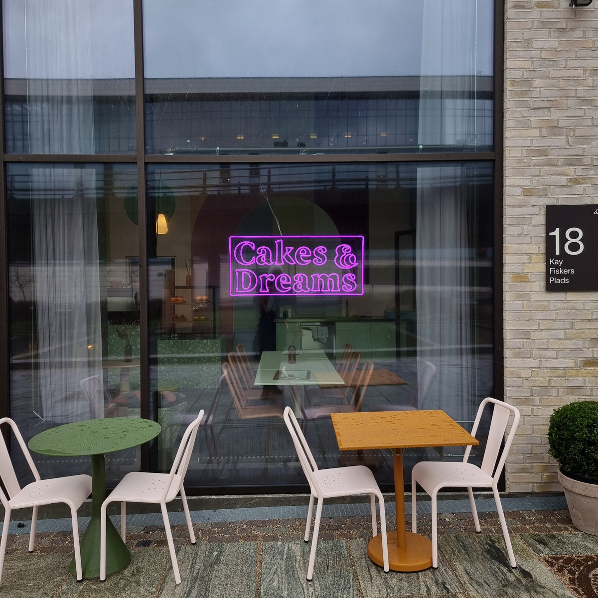 Pink neonskilt med Cakes &amp; Dreams i vinduet på en café