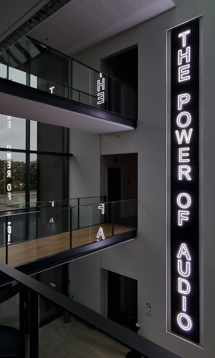Højt hvidt LED-neonskilt med teksten The Power of Audio i et moderne atrium