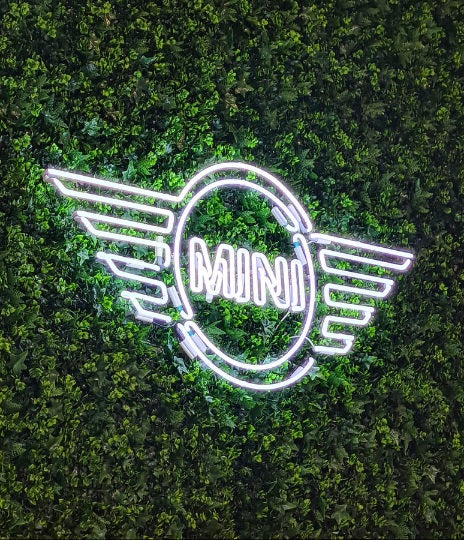 Hvidt LED-neonskilt med MINI-logoet på en grøn plantevæg